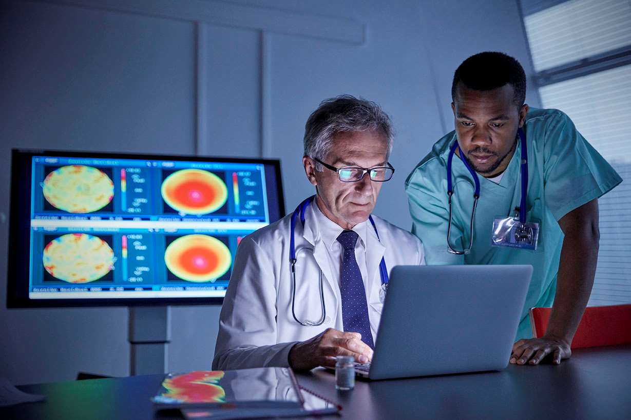 Medical staff consulting laptop with screen in background