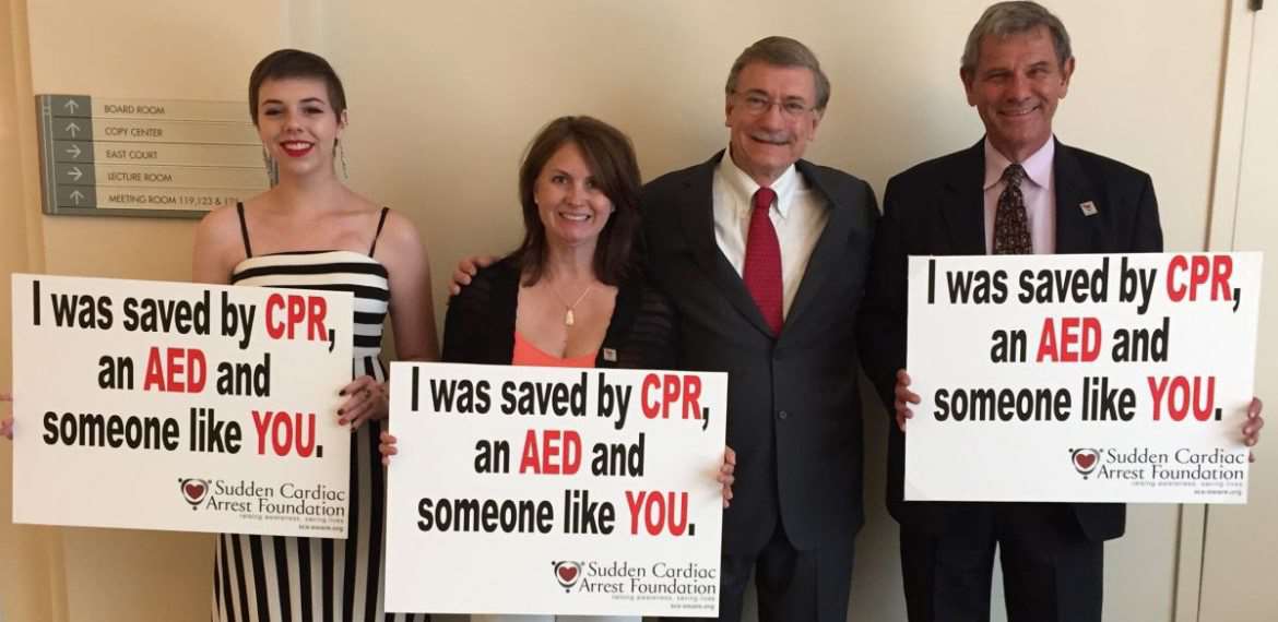 Three survivors of cardiac arrest standing next to Dr. Aufderheide hold signs that read, “I was saved by CPR, an AED and someone like YOU."