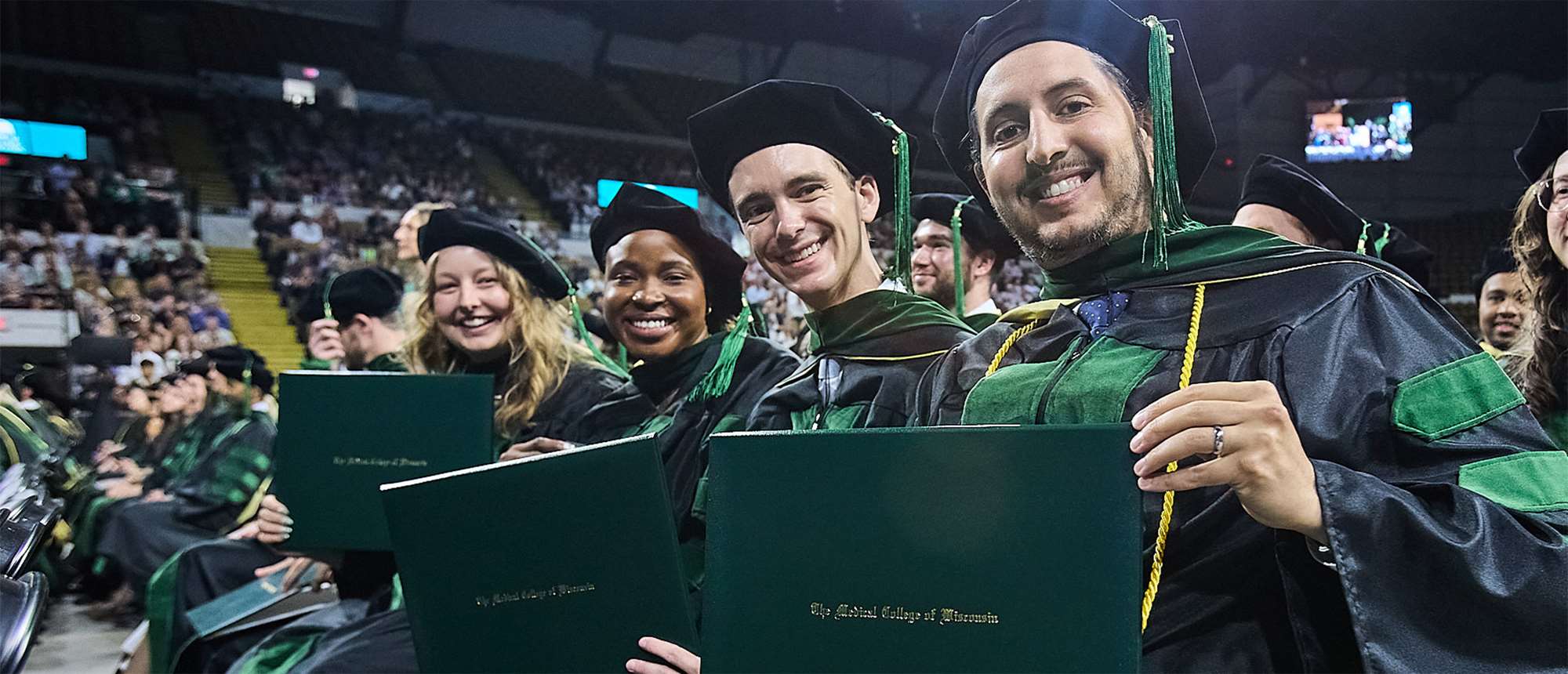 Four people holding diplomas at a graduation ceremony