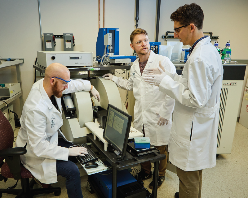 three students gathered around a piece of equipment