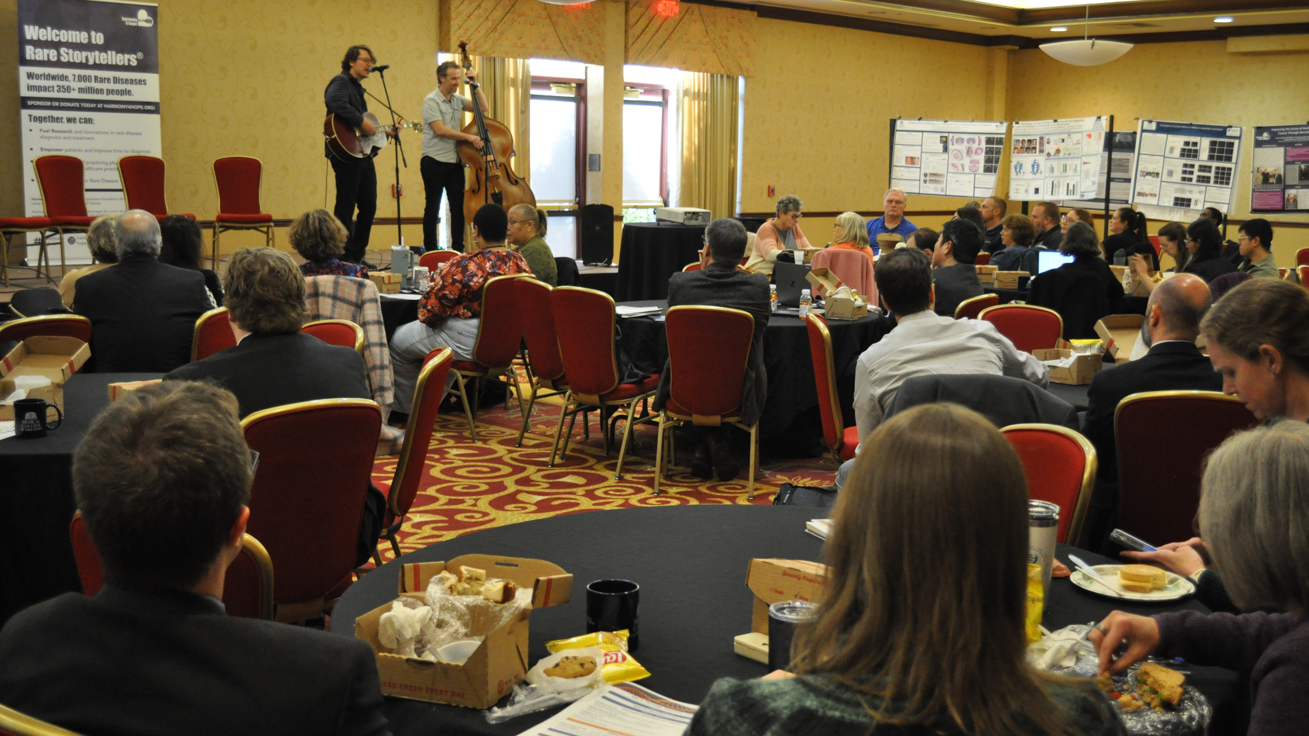 Musicians on stage in large conference room with crowd watching