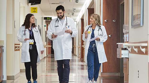 Three doctors in scrubs walking in hospital hallway