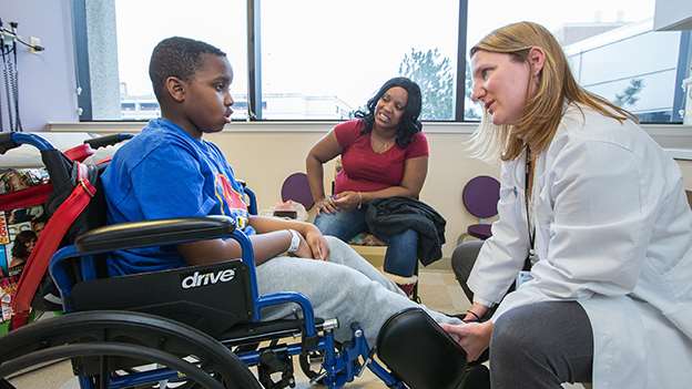 Female provider caring for young boy in wheelchair and consulting with mother