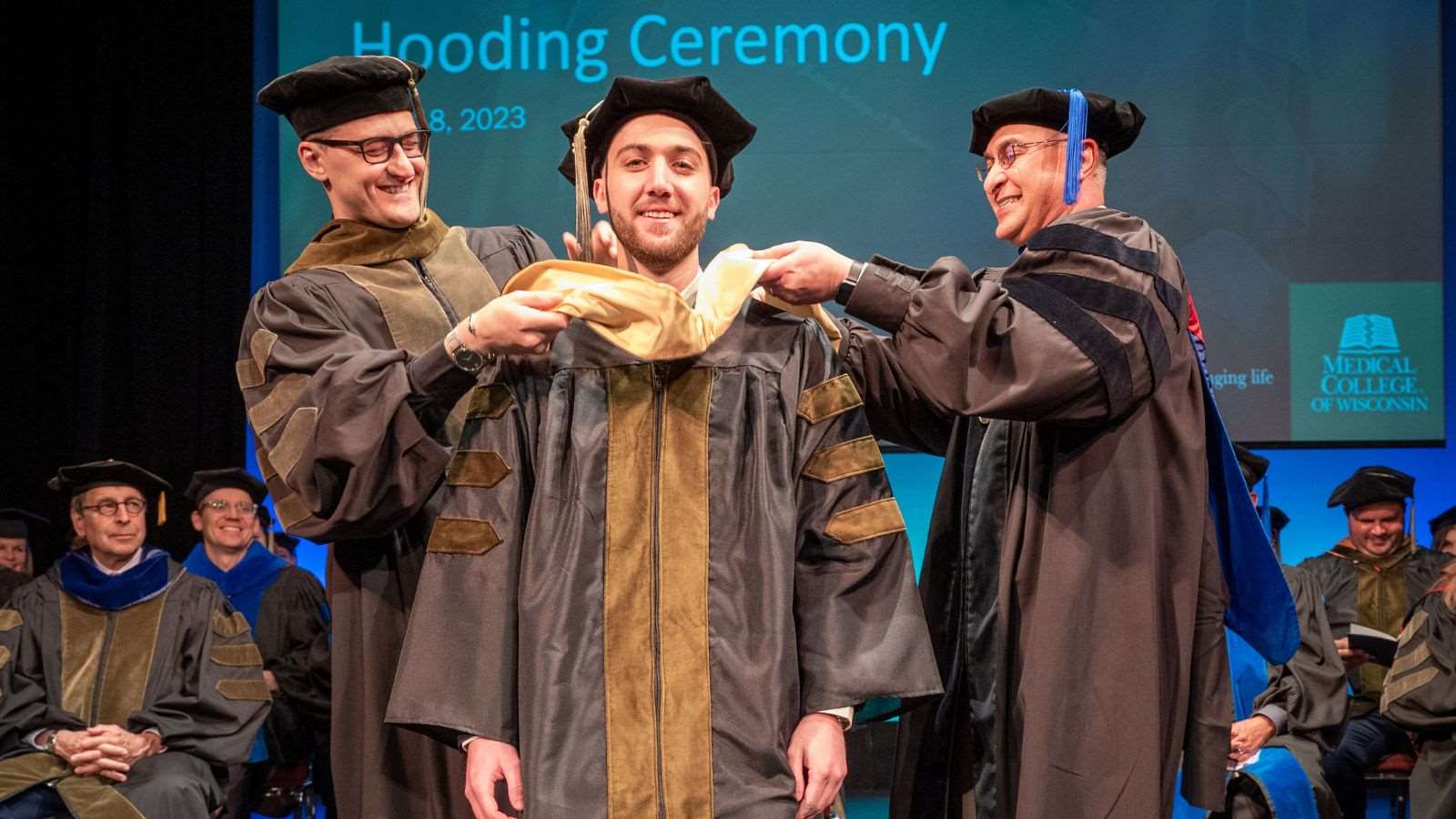 Accelerated_Intro Component Two faculty members place the PharmD academic hood around a graduating pharmacy student's shoulders