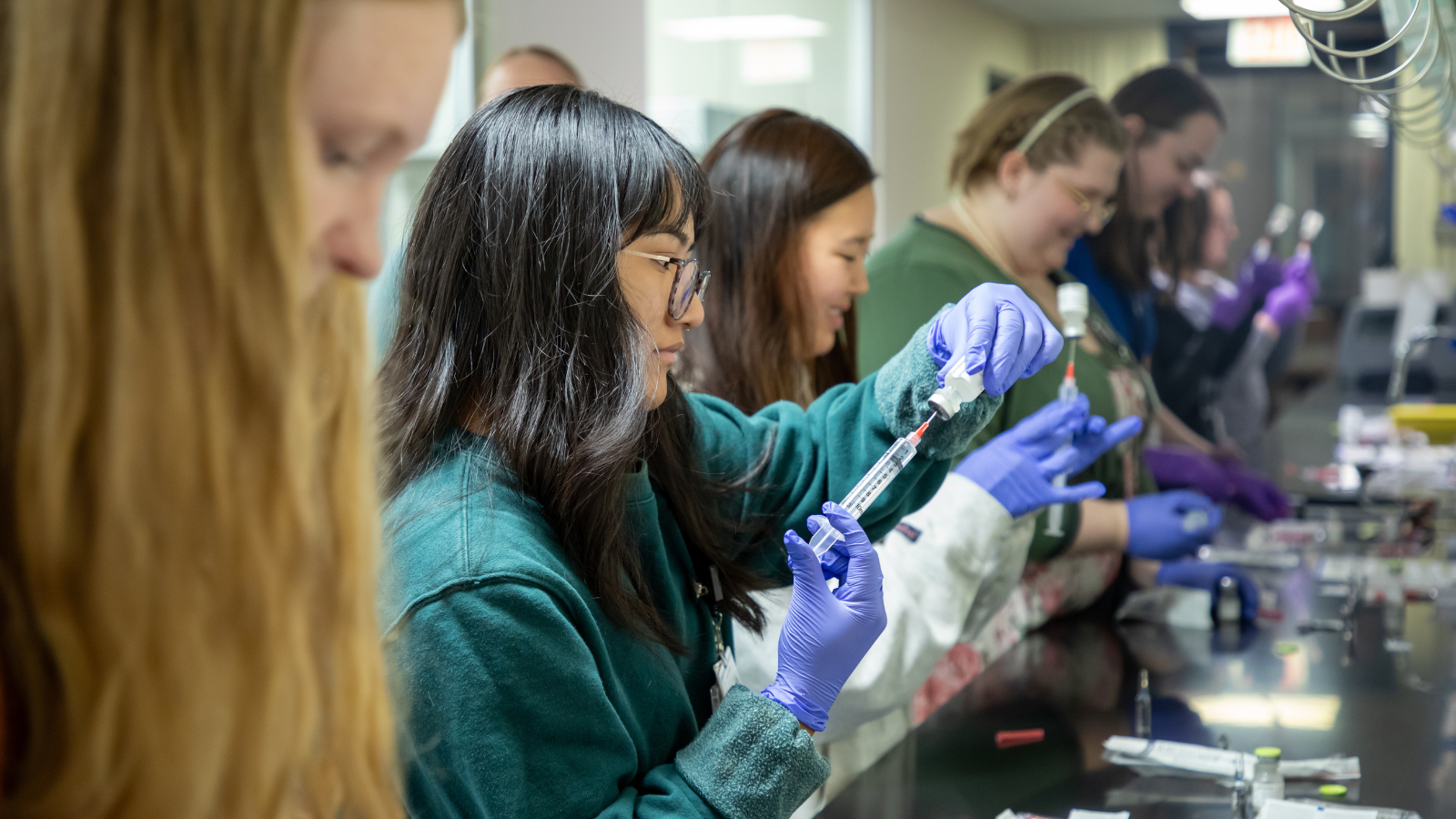 Multiple pharmacy students drawing medication into a syringe in a lab setting.