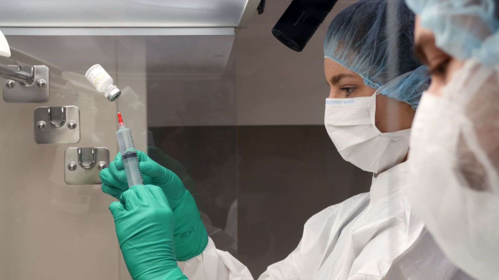 Person in the lab wearing PPE draws up a liquid into a syringe