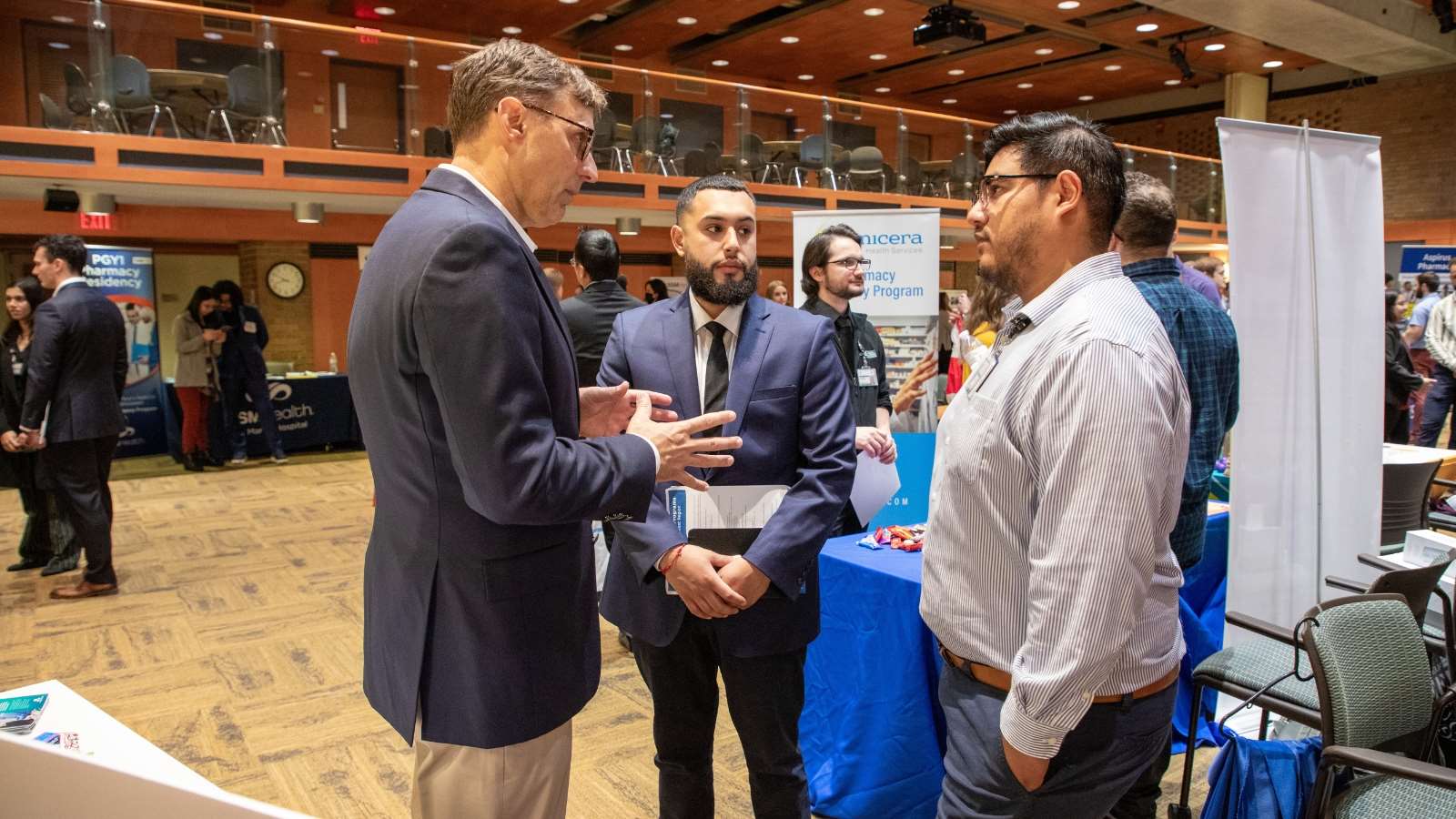 Events Page_Intro Component A pharmacy student and pharmacy resident speak with a pharmacist at an event.