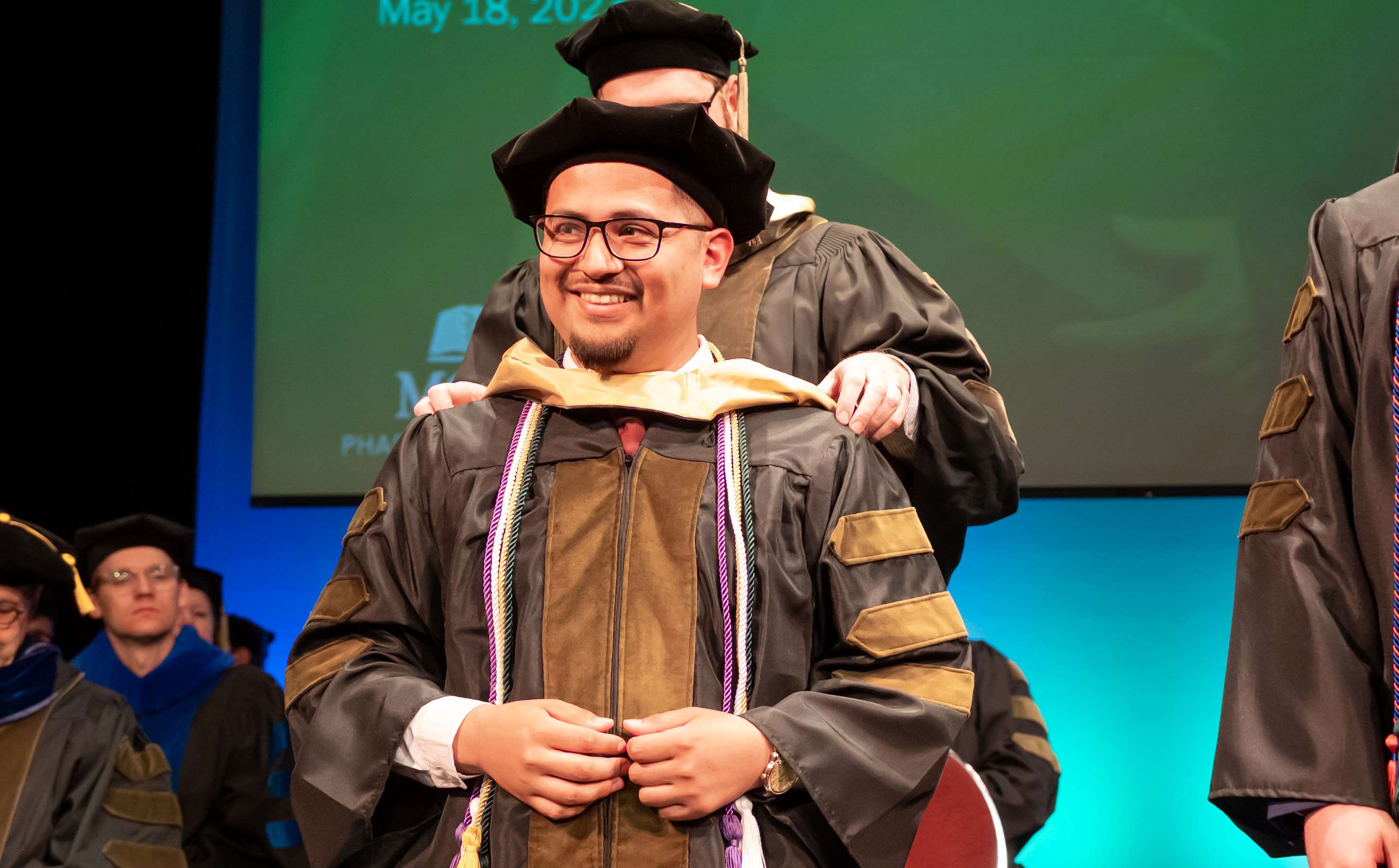 Student smiles at crowd during 2023 Hooding Ceremony, marking the achievement of his Doctor of Pharmacy degree.