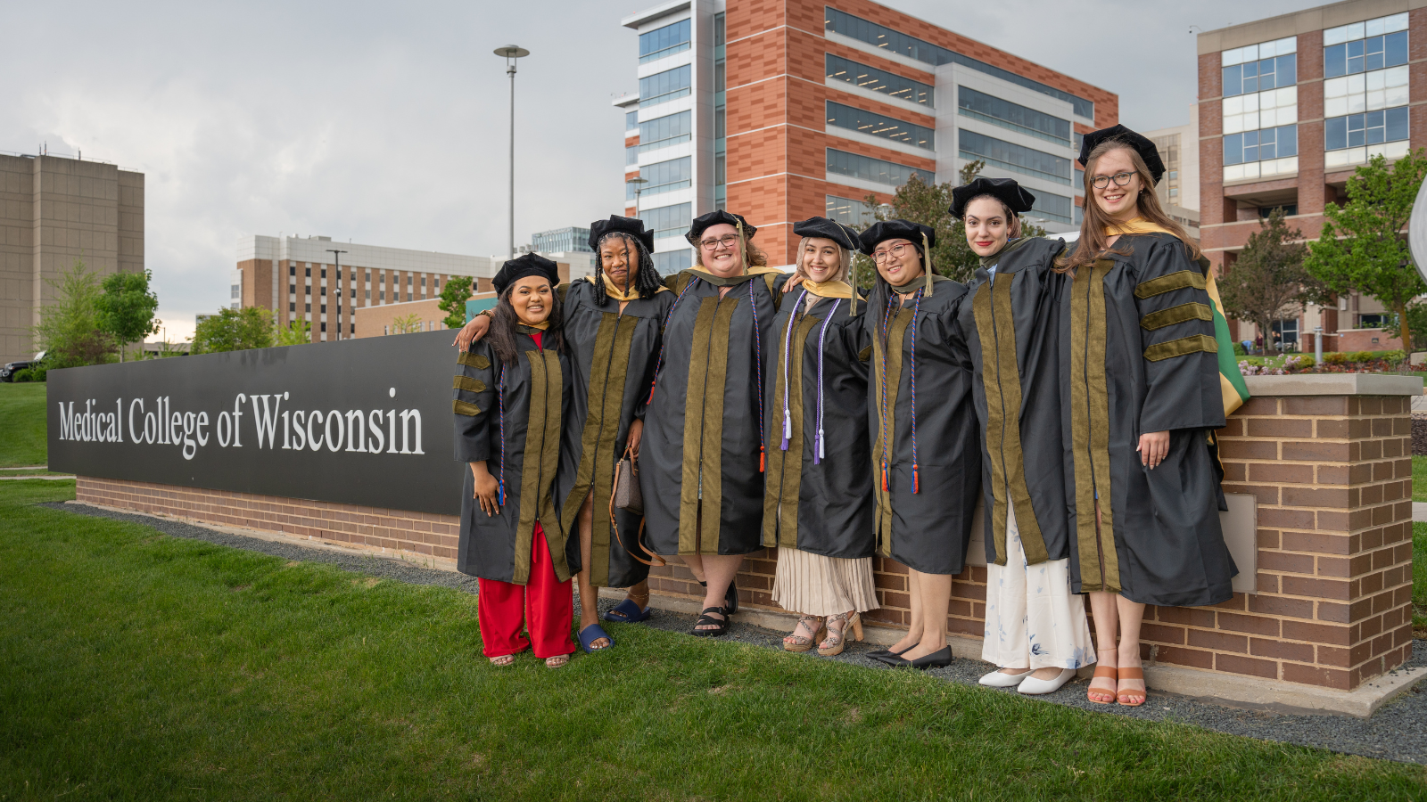 A group of Doctor of Pharmacy graduates stand in front of the Medical College of Wisconsin sign.