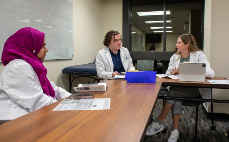 Medication Consultation_Image Card Three pharmacy students wearing white coats practice medication consultation skills.