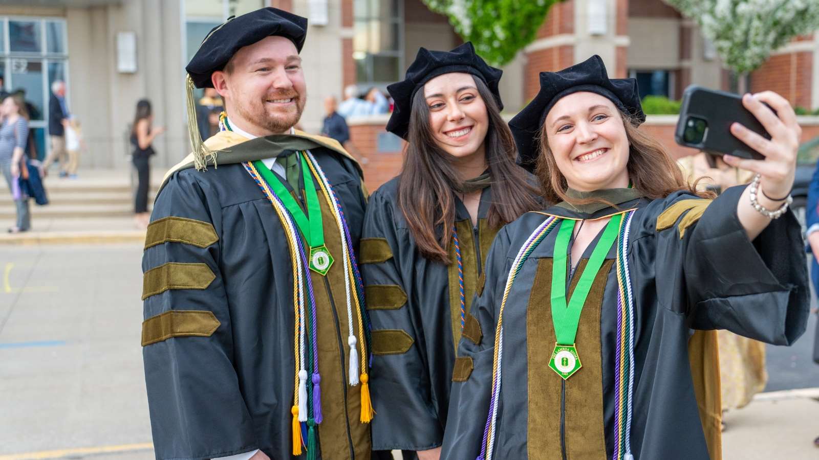 Three Doctor of Pharmacy graduates in graduation attire taking a selfie.