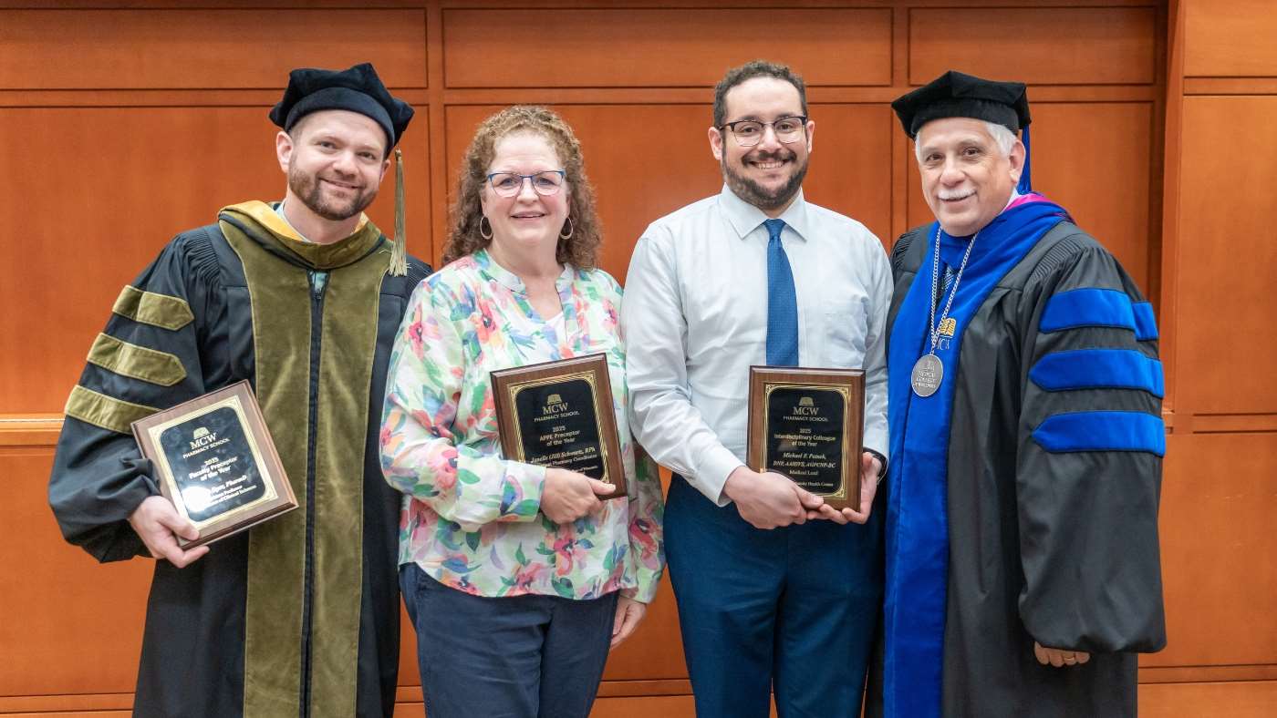 Three award winners holding plaques next to the MCW School of Pharmacy dean.