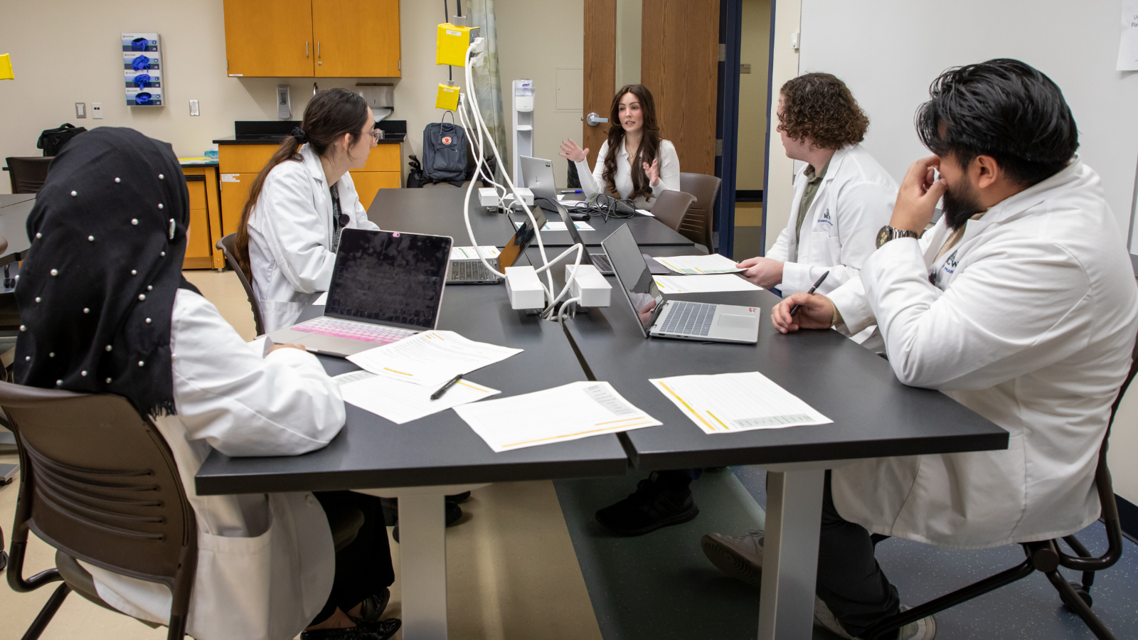 Community-Based Residency_Intro Component Pharmacy resident sits at a table, explaining a concept to a small group of students.