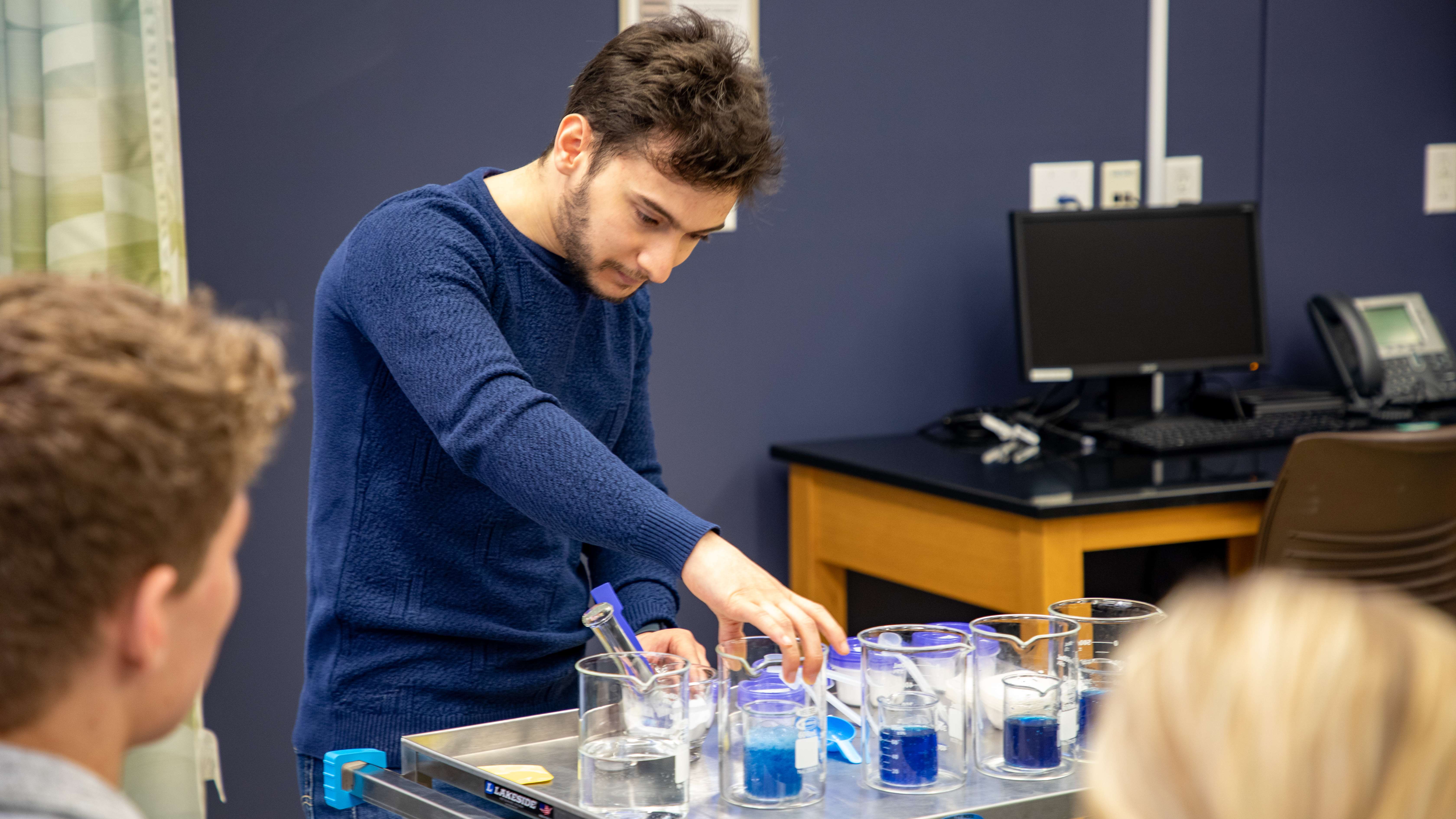 Male student experiments with beakers filled with blue liquid.