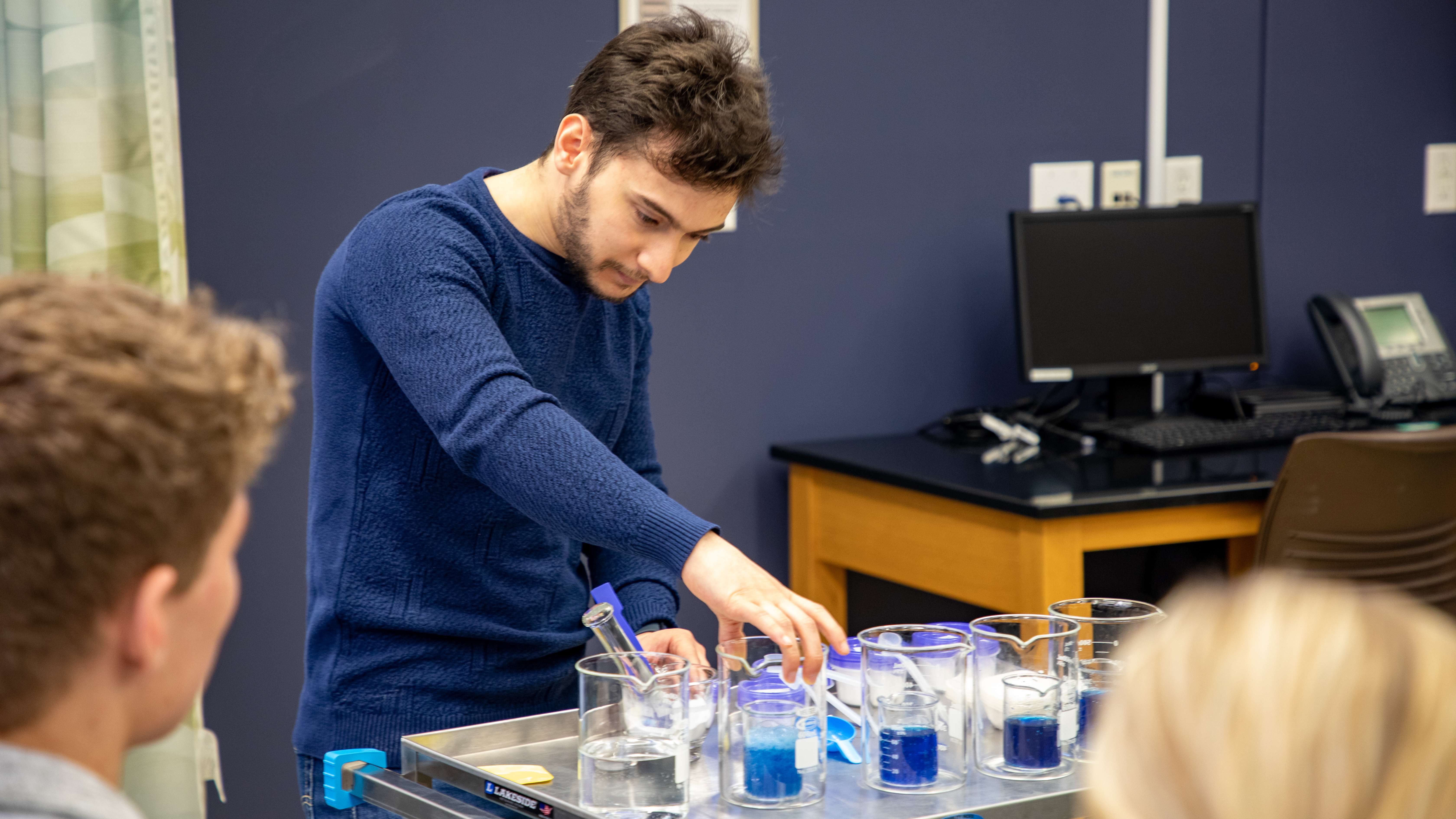 Experiment_Image Text Split Component Male student experiments with beakers filled with blue liquid.