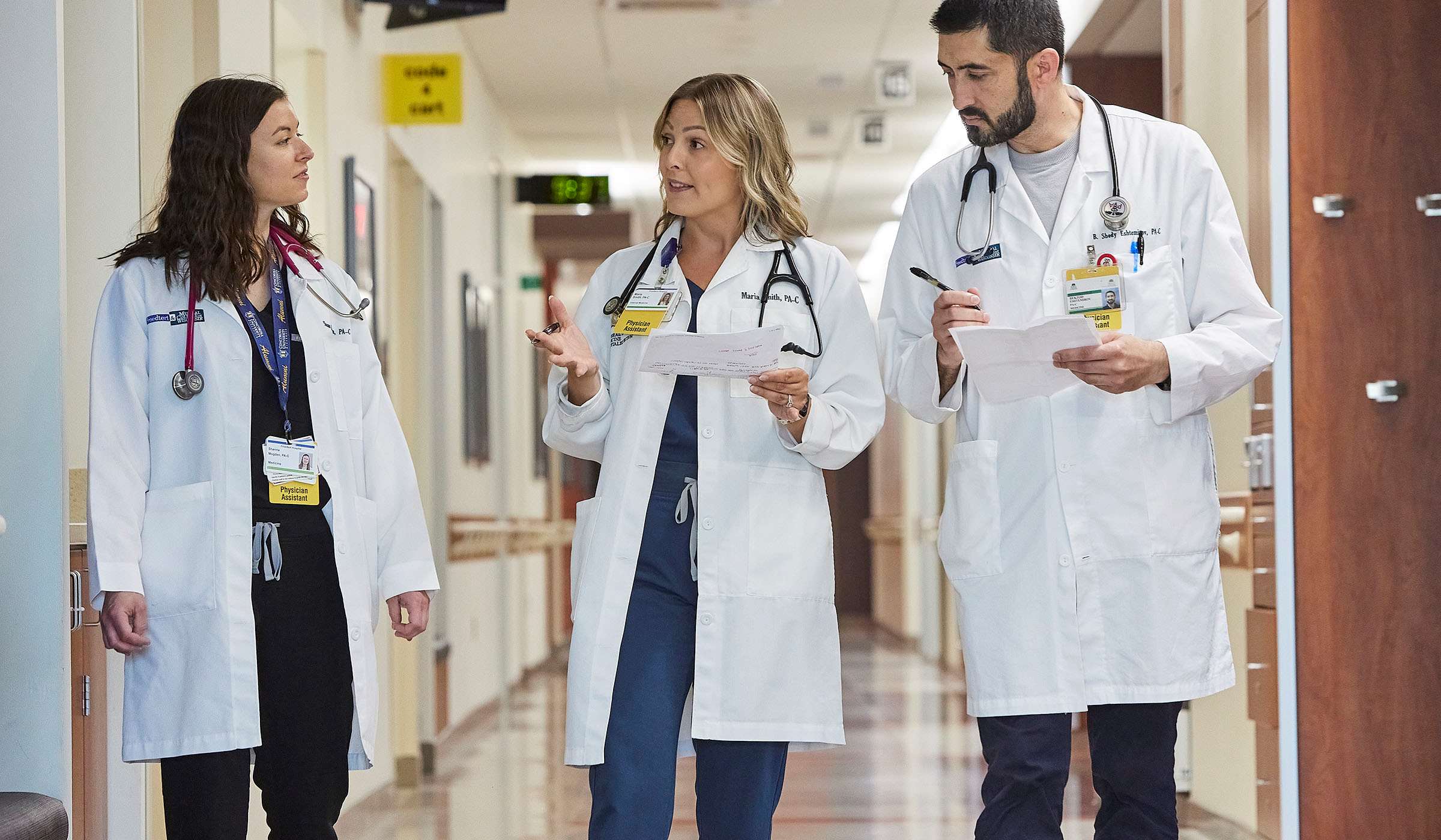 three people in white coats walking in hospital hallway
