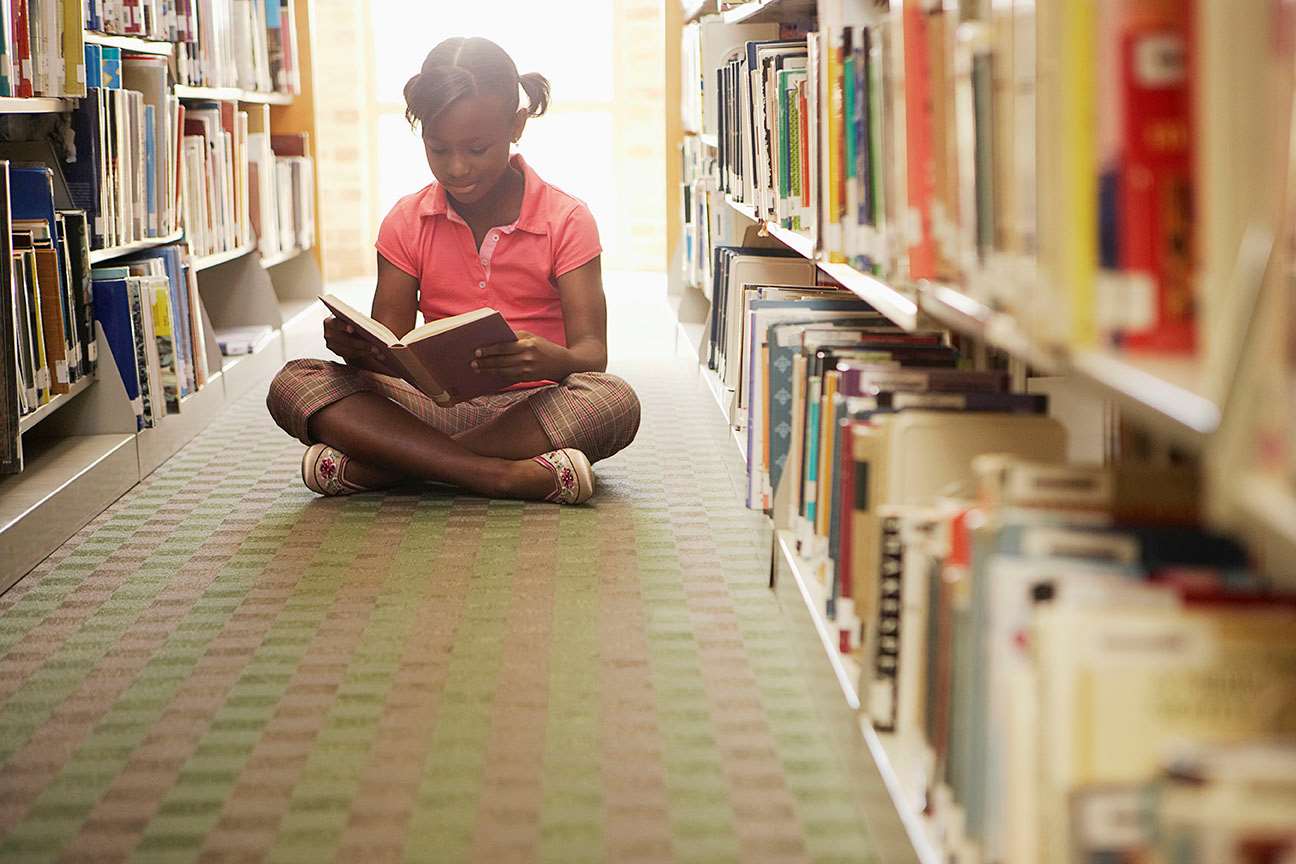 Young girl sitting reading books in library