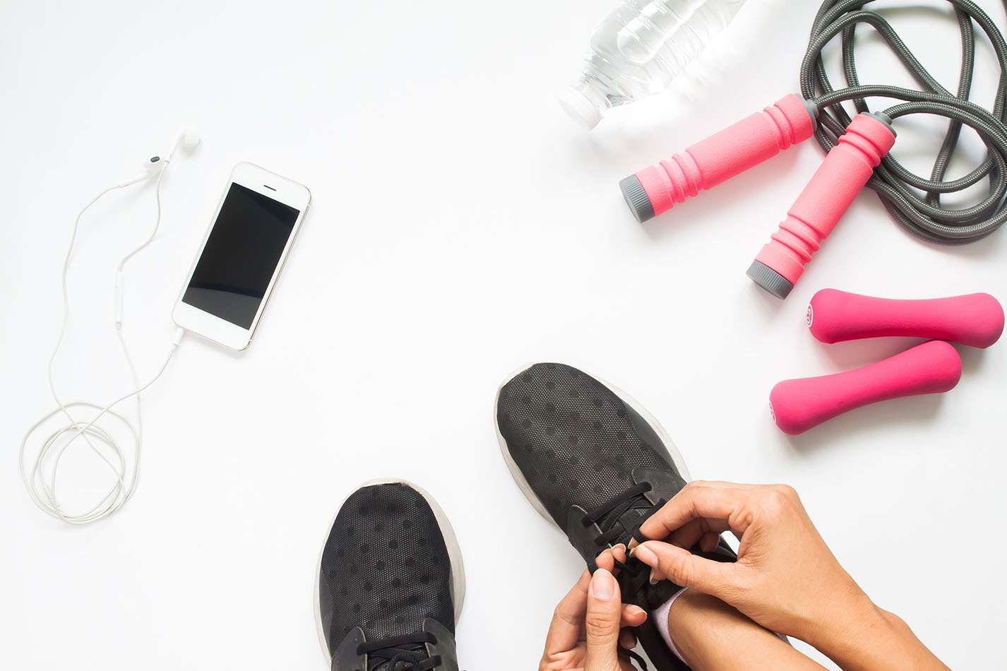 Hands tie shoes next to workout equipment