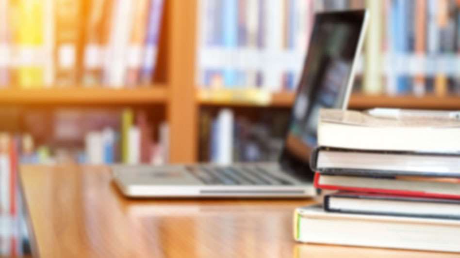 Laptop alongside books on desk in library