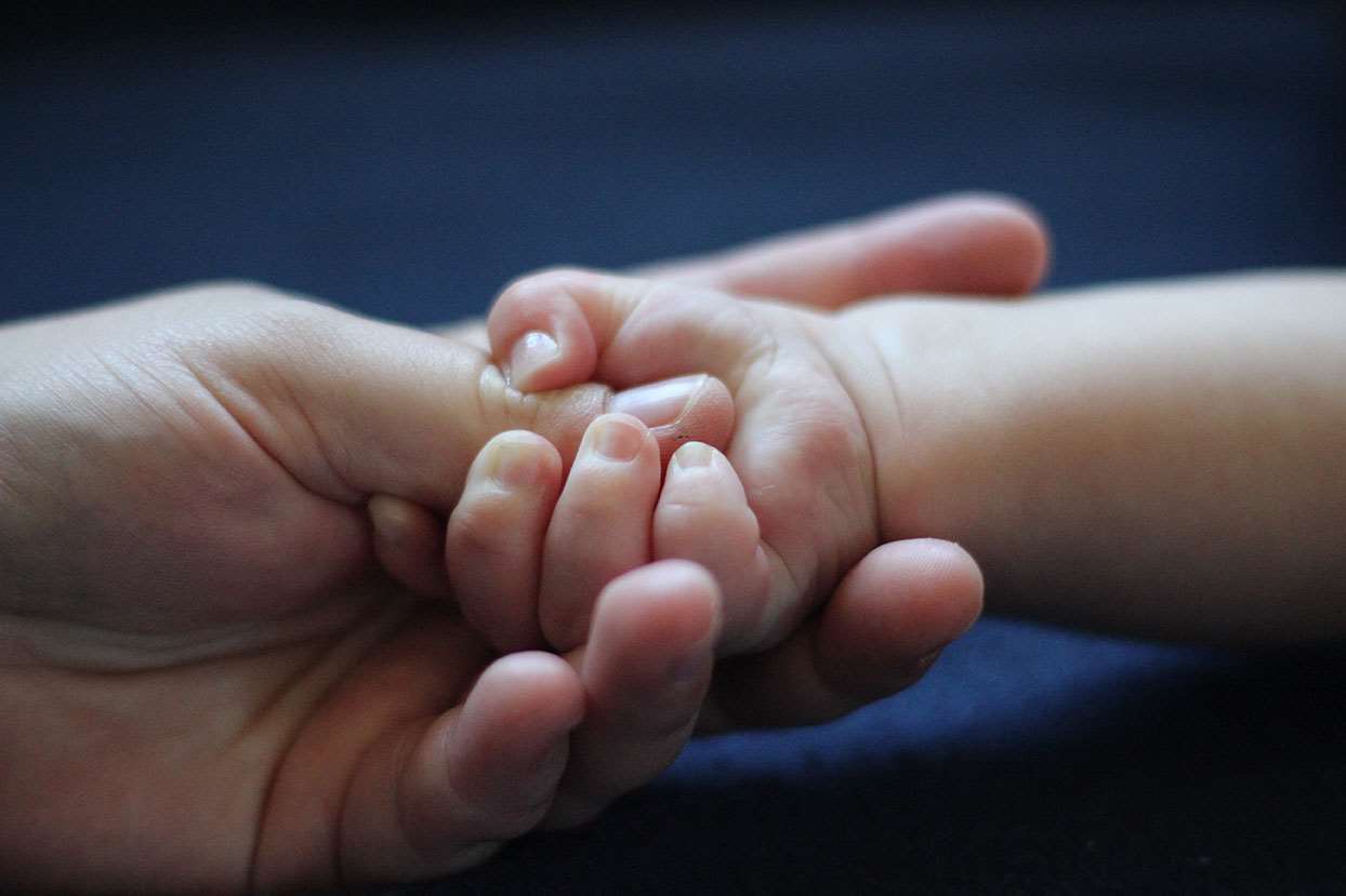Baby holding fingers of adult hand